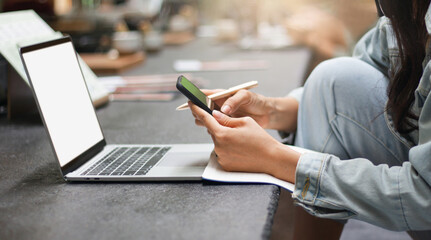 Focus on hand asian woman using mobile phone and wearing casual clothes working in cafe with laptop. Concept working or studying online with new normal