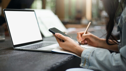 Focus on hand asian woman holding mobile phone and wearing casual clothes working in cafe with laptop. Concept working or studying online with new normal