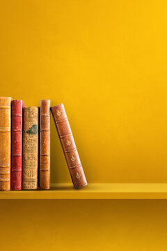 Row of old books on yellow shelf. Vertical background
