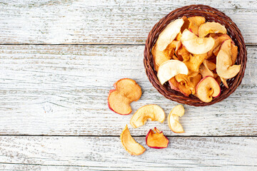 Fototapeta premium A pile of dried slices of apples in wicker basket on white wooden background. Dried fruit chips. Healthy food