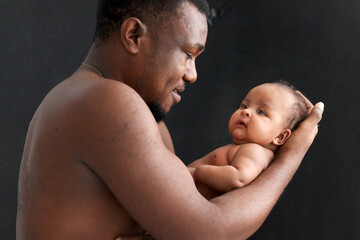 Little Asian African newborn baby girl in the embrace of her dad black background, portrait of sweet adorable infant in arms of father, parent holding baby.
