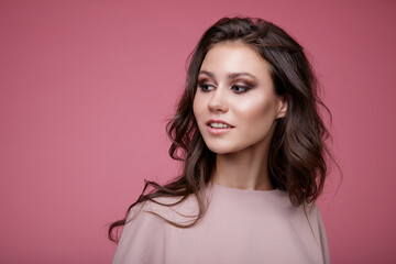 High fashion photo of a beautiful elegant young woman in a pretty pink jumpsuit posing on pink background. Slim figure. Studio Shot. Luxurious hair, shiny curls. Femininity and tenderness. Monochrome