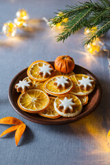 Dried oranges and ginger cookie on a brown plate. Winter seasonal treats and decoration with pine branch an a shiny garland. Soft selective focus