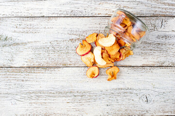 A pile of dried slices of apples pills out of a glass jar on white wooden background. Dried fruit chips. Healthy food