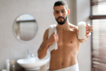 Handsome young guy standing with deodorant bottle in hand - obrazy, fototapety, plakaty