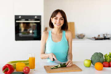 Happy fit lady cooking healthy vegetable salad, cutting cucumber on wooden board, preparing food and smiling at camera