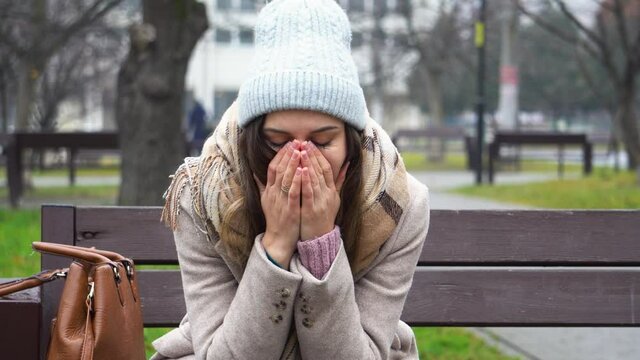Young woman sitting on a park bench in a depressed and bad mood.