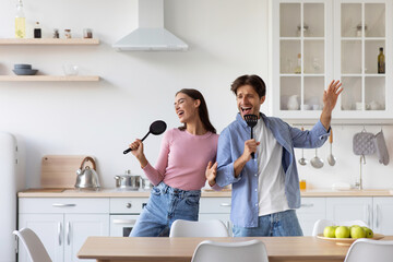 Happy glad european young guy and lady sing into virtual microphones together in kitchen interior