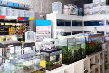 Interior of pet store with various of bird cages, shelves with pet accessories, rows of aquariums...