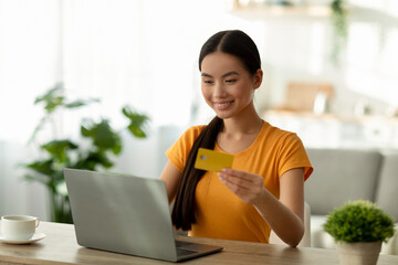 Positive asian lady shopping online, using credit card and laptop, transferring money, ordering...