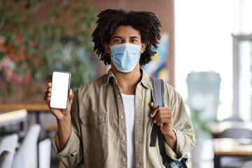 Safety Measures. Black Guy Wearing Medical Mask Showing Blank Smartphone At Cafe