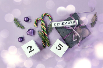 Calendar for December 25: name of the month in English, number 25 on cubes, Christmas decorations, festive caramel, padarok tied with a pastel ribbon on a pastel background, top view