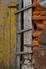 Old red brick wall. With elements of wooden boards with remnants of yellow peeling paint.