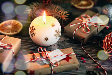 Naklejka na ściany i meble Christmas home decoration, burning candle close-up on a dark wooden background and gifts in craft paper