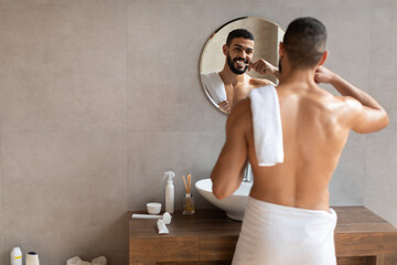 Happy young Arab man using toothbrush in modern bathroom