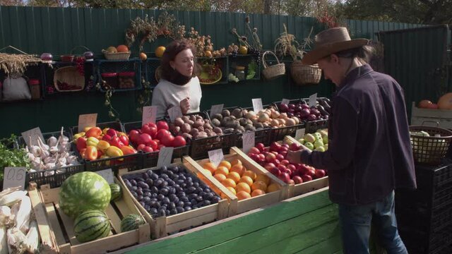 Buying red apples at the market. Shooting in two cameras. 2 Shots. A man buys apples at the farmers' market. A woman seller gives him a plastic bag and he puts apples in it. The customer pays in cash.