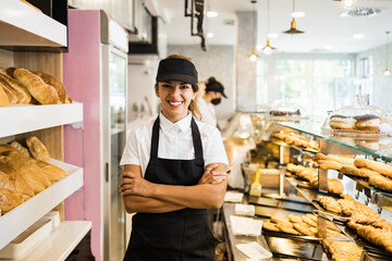 Beautiful young and happy female worker working in a modern bakery. She is posing and looking at camera with corssed rms.