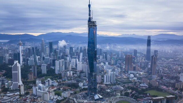 Aerial drone time lapse of Kuala Lumpur city skyline with low rolling clouds. Zoom out