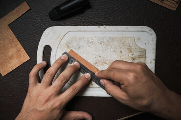Top view of a man's hands cutting a sheet of cork.