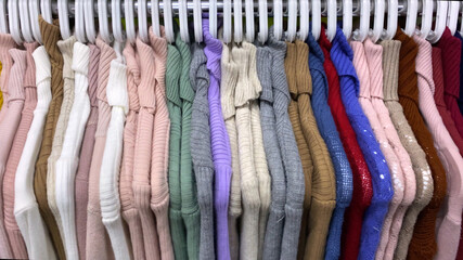 women jumpers in different colors, clothes on hangers in shop