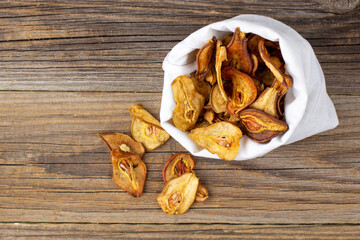 A pile of dried slices of pears in white pouch on wooden background. Dried fruit chips. Healthy food