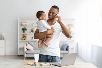 Multitasking Concept. Young Black Man Holding Little Baby And Talking On Cellphone