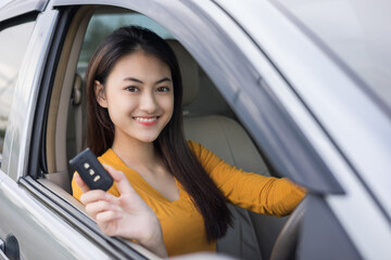 Young beautiful asian women getting new car. she very happy and excited looking outside window in hand holding car key. Smiling female driving vehicle on the road on a bright day