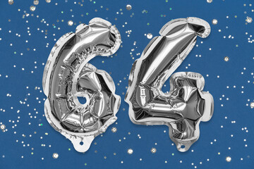 Silver foil balloon number, digit sixty four on a blue background with sequins. Birthday greeting card with inscription 64. Top view. Numerical digit. Celebration event, template.