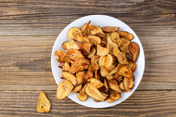 A pile of dried pears in slices on a white plate on wooden background. Dried fruit chips. Healthy food