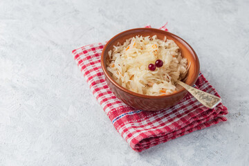 Sauerkraut or pickled cabbage in in a clay bowl on a red napkin close up on a light table with copy space