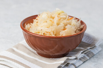 Sauerkraut or pickled cabbage in in a clay bowl on a napkin close up on a light table