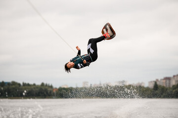 young energetic woman extreme jumping over the splashing wave on wakeboard