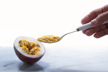 Woman's hand scooping fresh ripe Passion fruit with spoon, white background