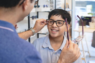 Happy Indian father and son choosing eyeglasses frames in optical store