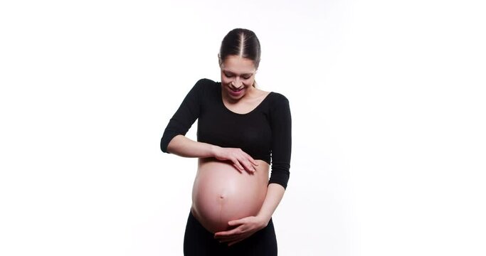 Happy young and fit pregnant woman gently smile and soft strokes her tummy while waiting for a baby, isolated on white background. Happy, healthy and touching pregnancy soulful moments concept