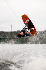 Naklejka premium sportive energetic woman holds rope and doing flips and jumping over the water on wakeboarding board