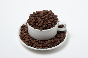 White cup overflowing with coffee beans on a white background. Freshly roasted coffee beans