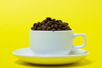 Cup filled with coffee beans on a yellow background. Freshly roasted coffee beans. Excessive consumption of caffeine