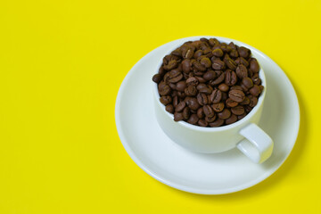 Cup filled with coffee beans on a yellow background. Freshly roasted coffee beans. Excessive consumption of caffeine