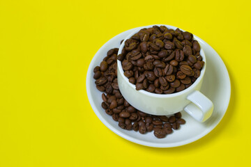 Cup filled with coffee beans on a yellow background. Freshly roasted coffee beans. Excessive consumption of caffeine
