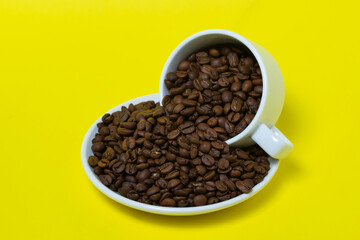 Cup filled with coffee beans on a yellow background. Freshly roasted coffee beans. Excessive consumption of caffeine