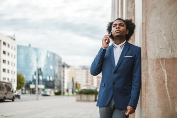 african american young man in suit in a work call with his cellphone outdoors