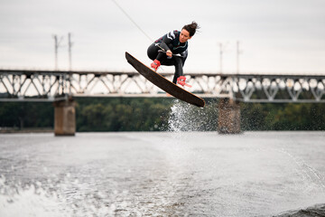 Naklejka premium young woman holding rope and professionally jumping over splashing water on wakeboarding board