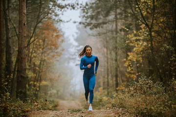 Young woman running toward camera on the forest trail at autumn