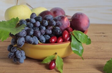 There are grapes, dogwood, plums and apples in a clay bowl.	