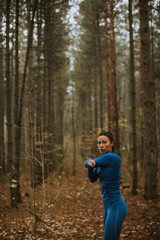 Naklejka na ściany i meble Young woman in blue track suit stretching before workout in the autumn forest