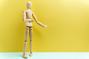 Wooden mannequin shows a presentation on the wall. Yellow background. Space for copying text
