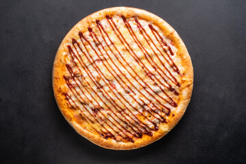 Round baked pizza with tomato, pepper, sausage, cheese on a black background. 