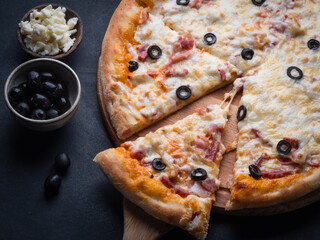 Home pizza with sausage, cheese, olive, pepper, Spices on black background. Supreme Hot Pizza