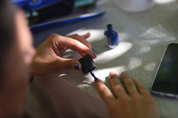 Woman painting her nails blue in detail shot